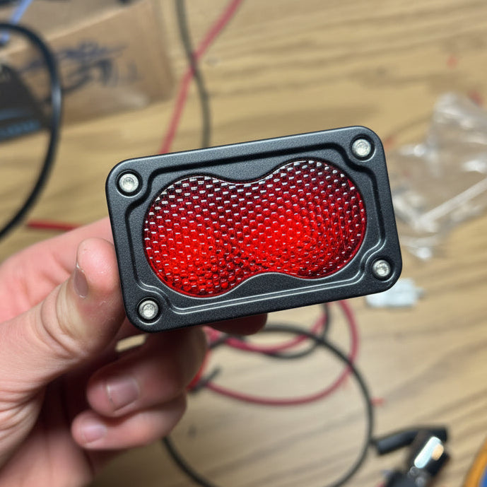 Red LED light held by a hand on a cluttered workbench with tools and components.
