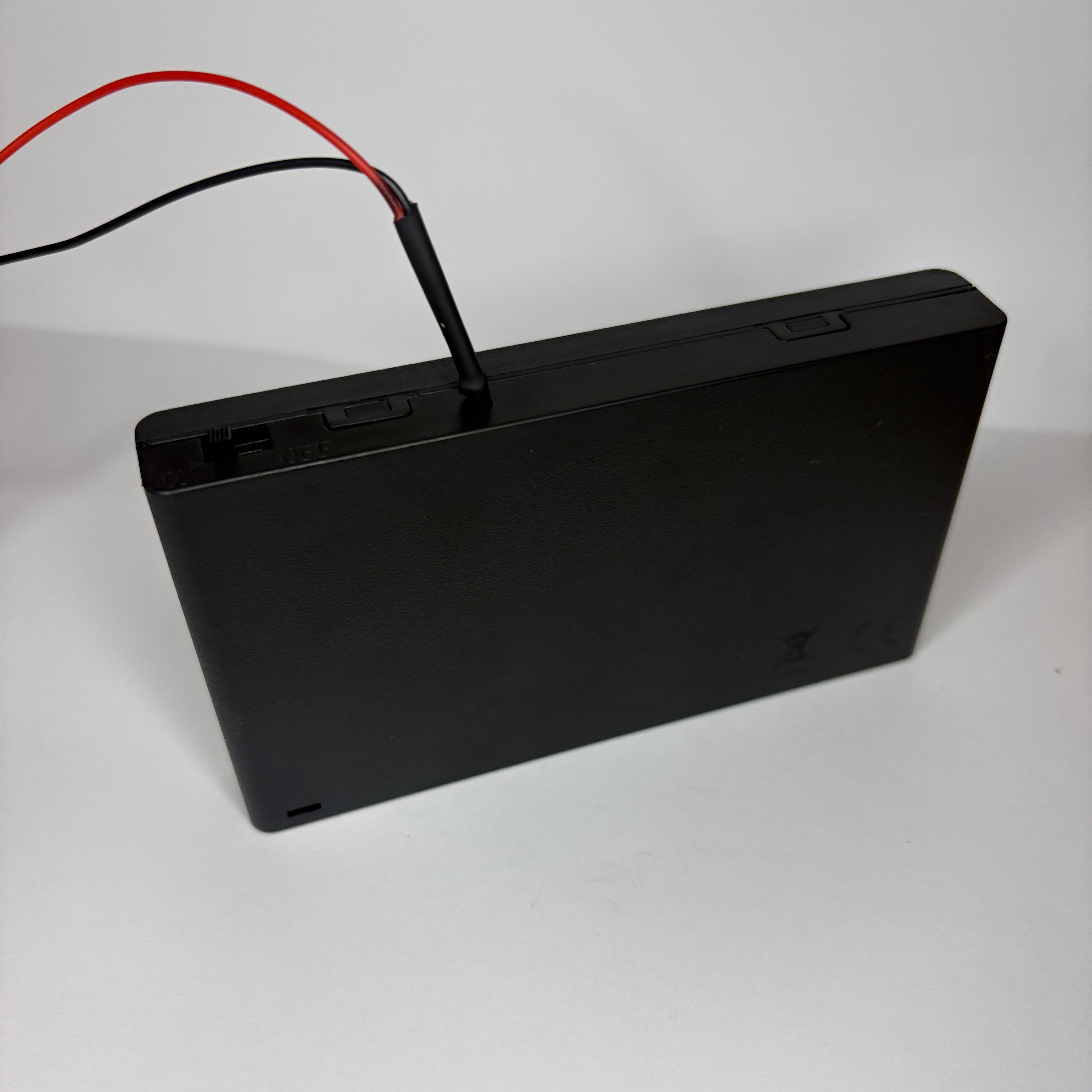 Black electronic device with red and black wires on a white background